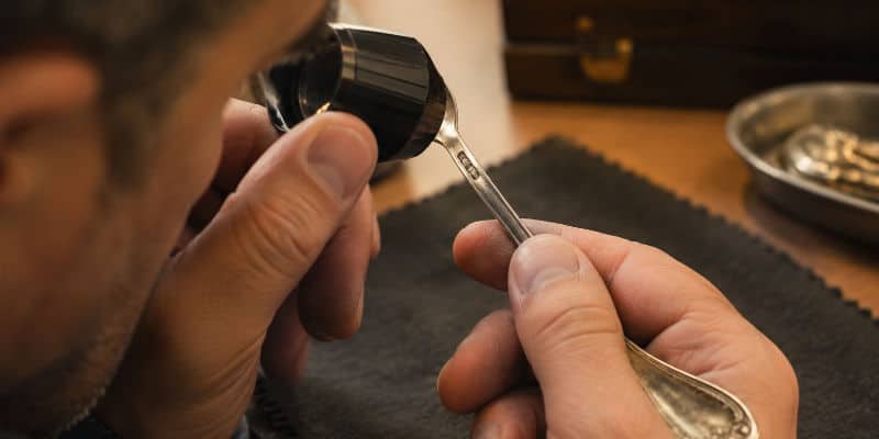 Examen à la loupe d'un poinçon sur une pièce d'argenterie ancienne
