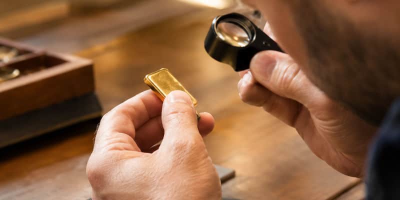 Professionnel examinant un lingot d'or à la loupe pour en vérifier l'authenticité